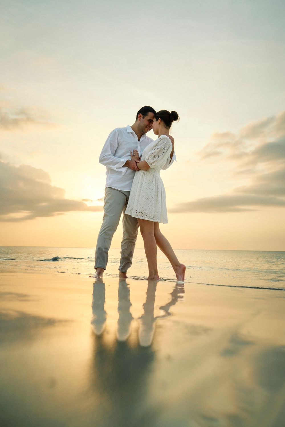 Romantic silhouette of couple embracing on beach at sunset with reflection in wet sand.
