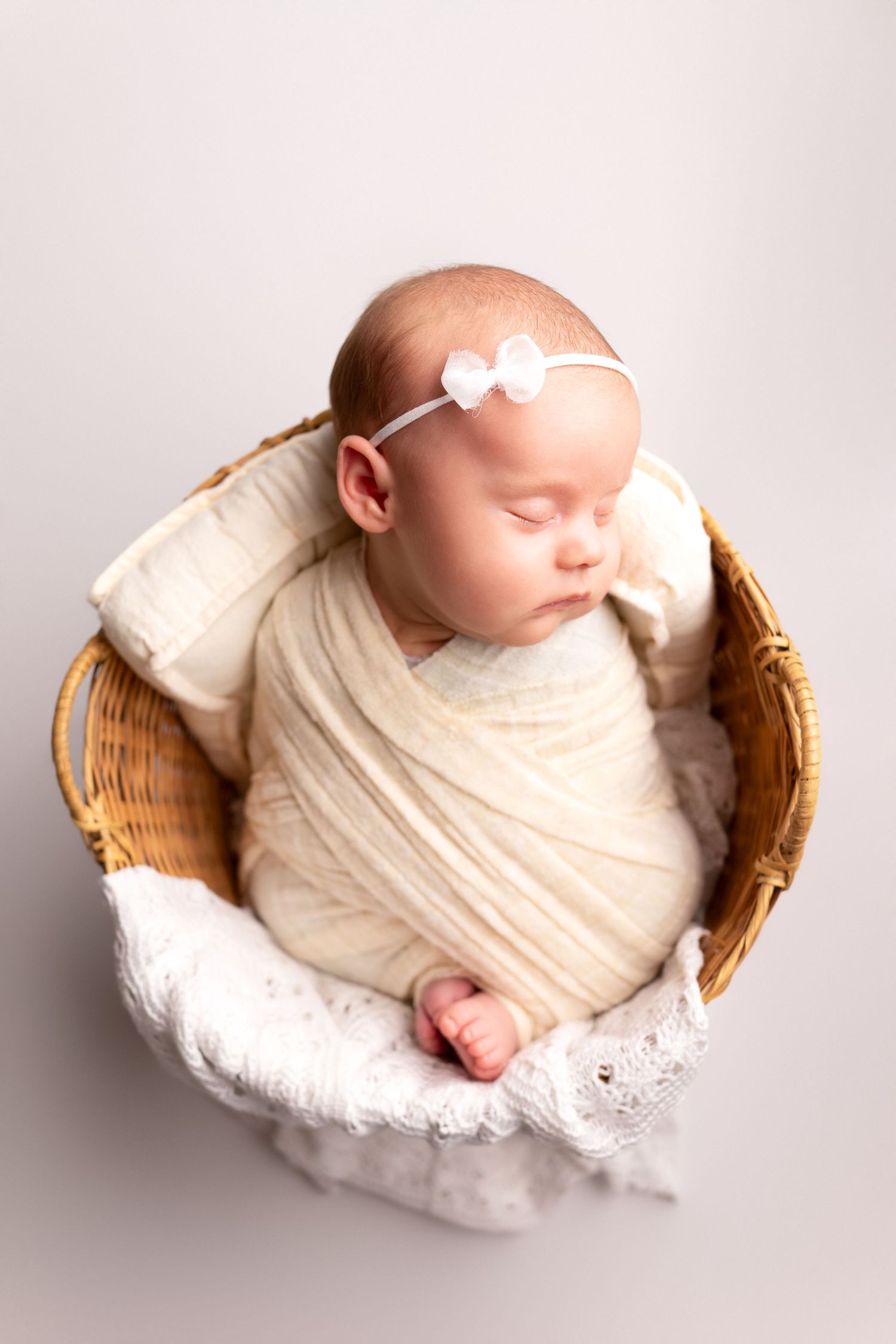 Sleeping newborn wrapped in cream fabric resting in woven basket.