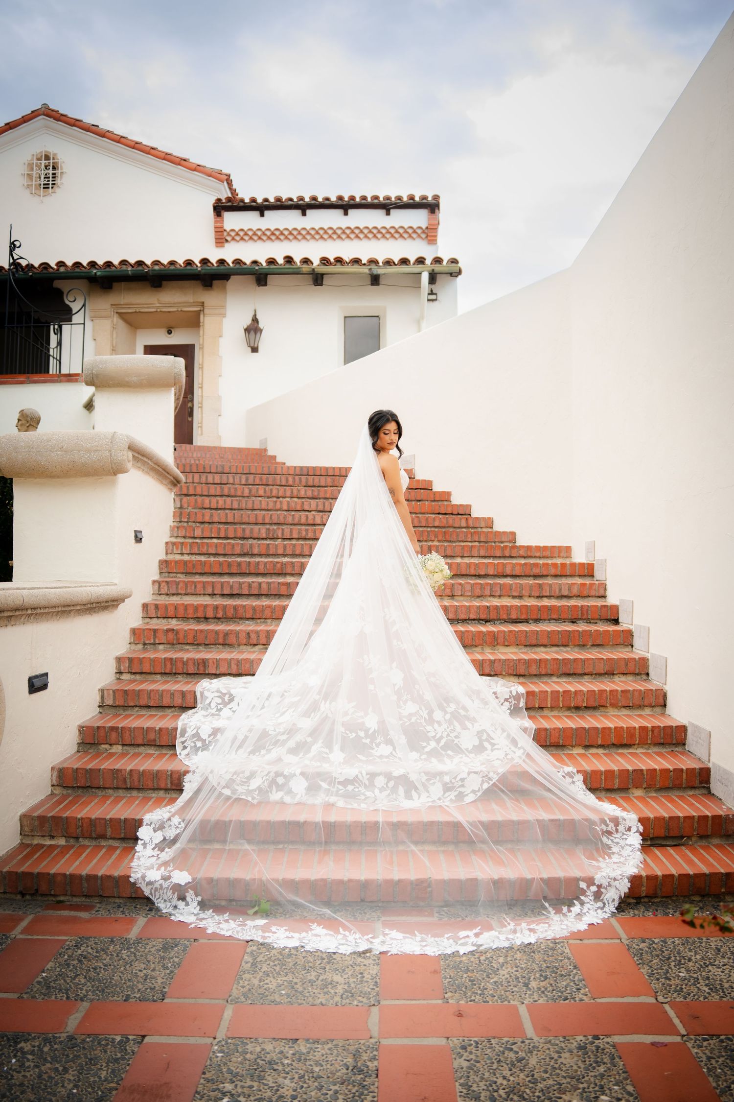 A dramatic bridal portrait series on terracotta stairs showcasing a flowing cathedral veil and white wedding gown.