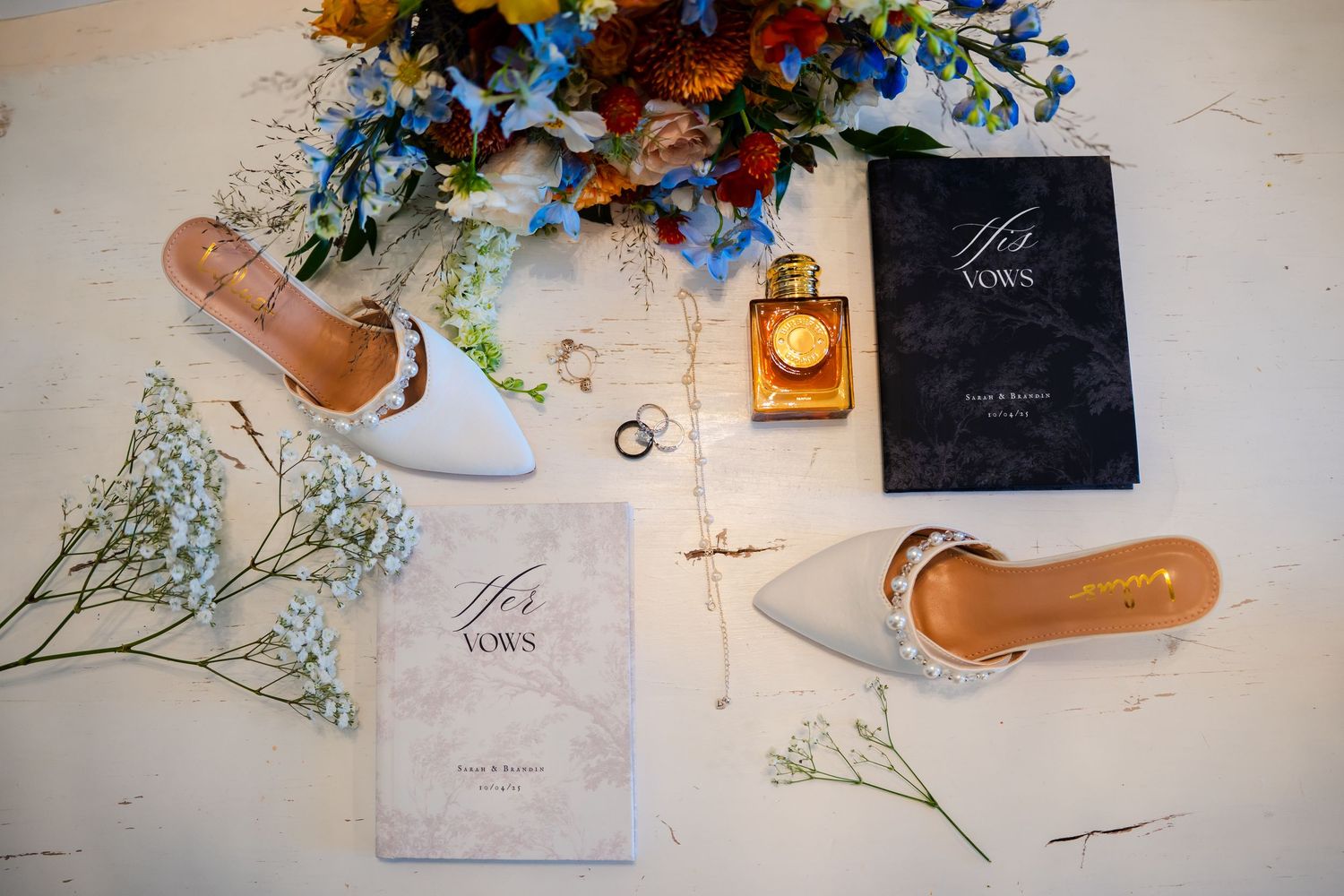 Flat lay composition of perfume bottles, dried flowers, and beauty products arranged on a white surface.