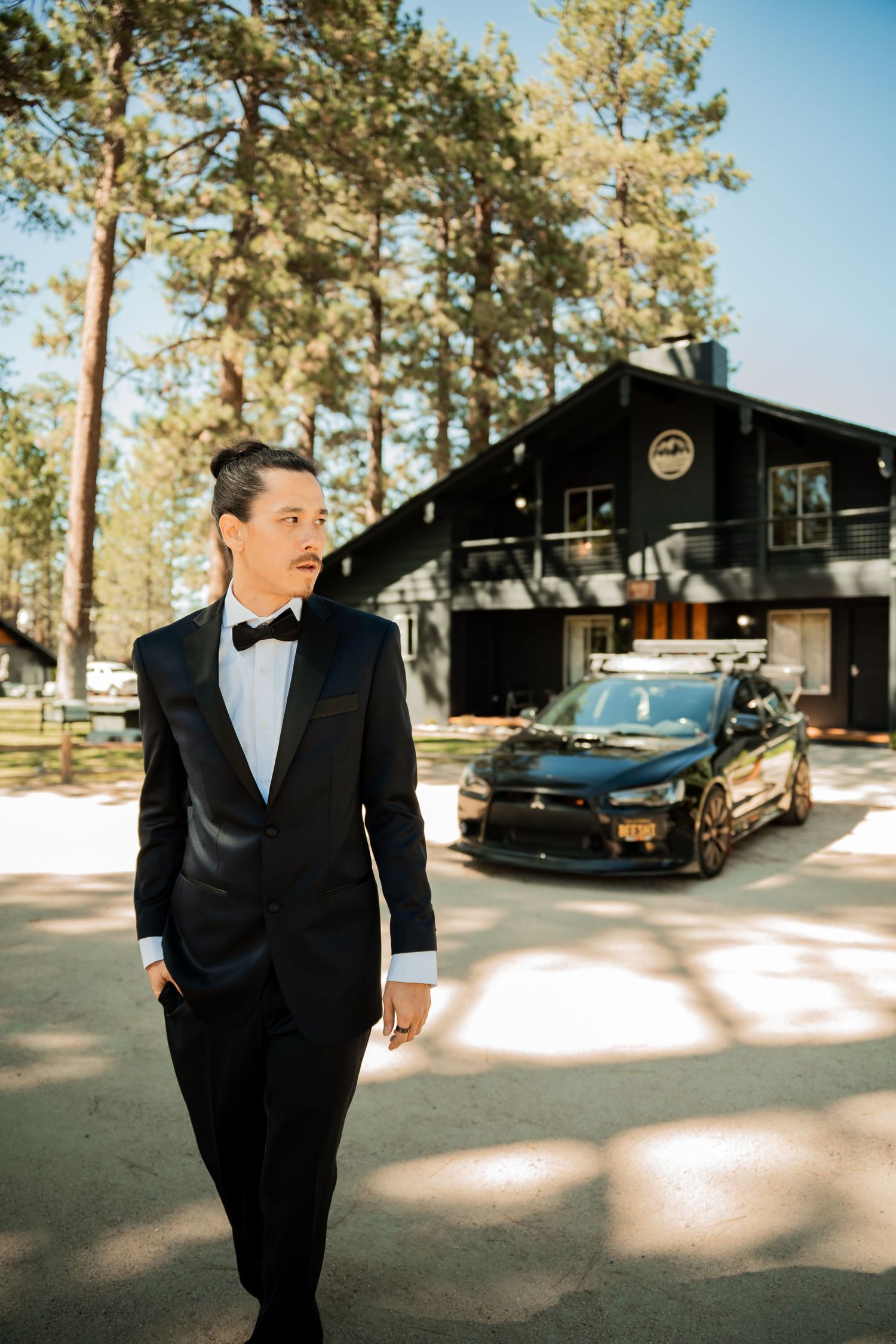 A series of five photos showing someone in a black tuxedo walking outside a rustic cabin venue on a sunny day.