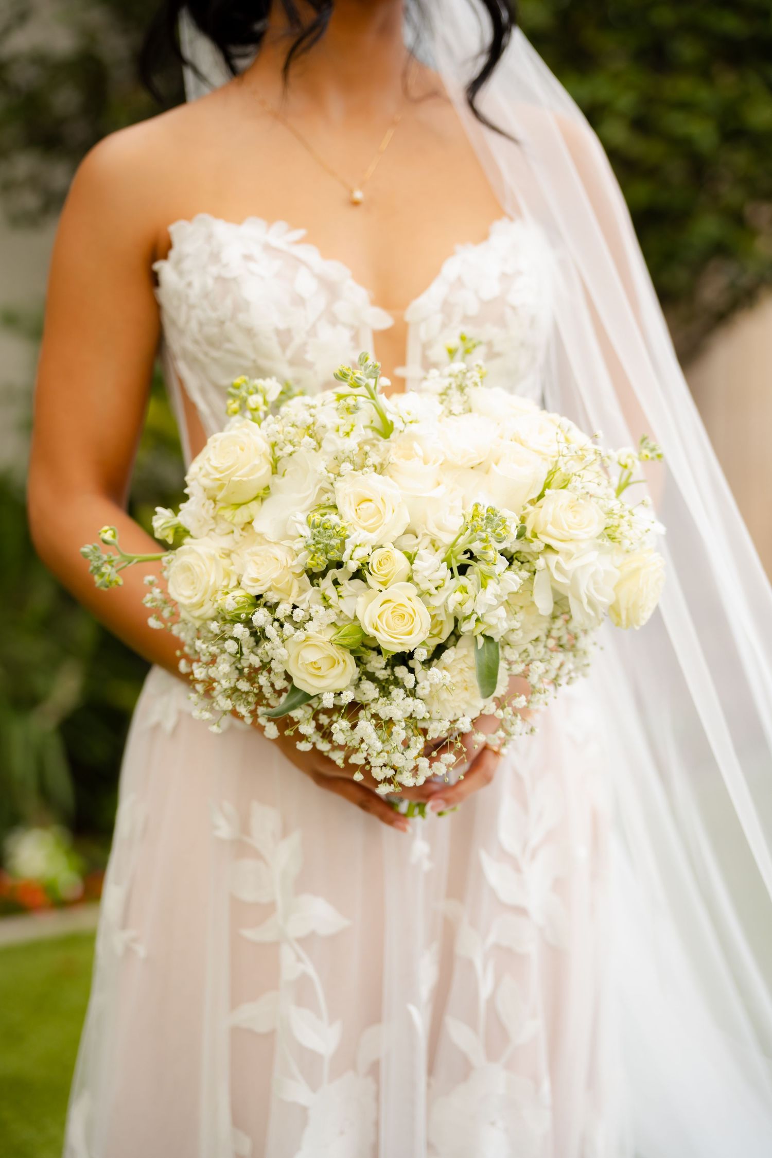 Close-up of an elegant bridal bouquet featuring white roses and baby's breath against a flowing wedding dress.