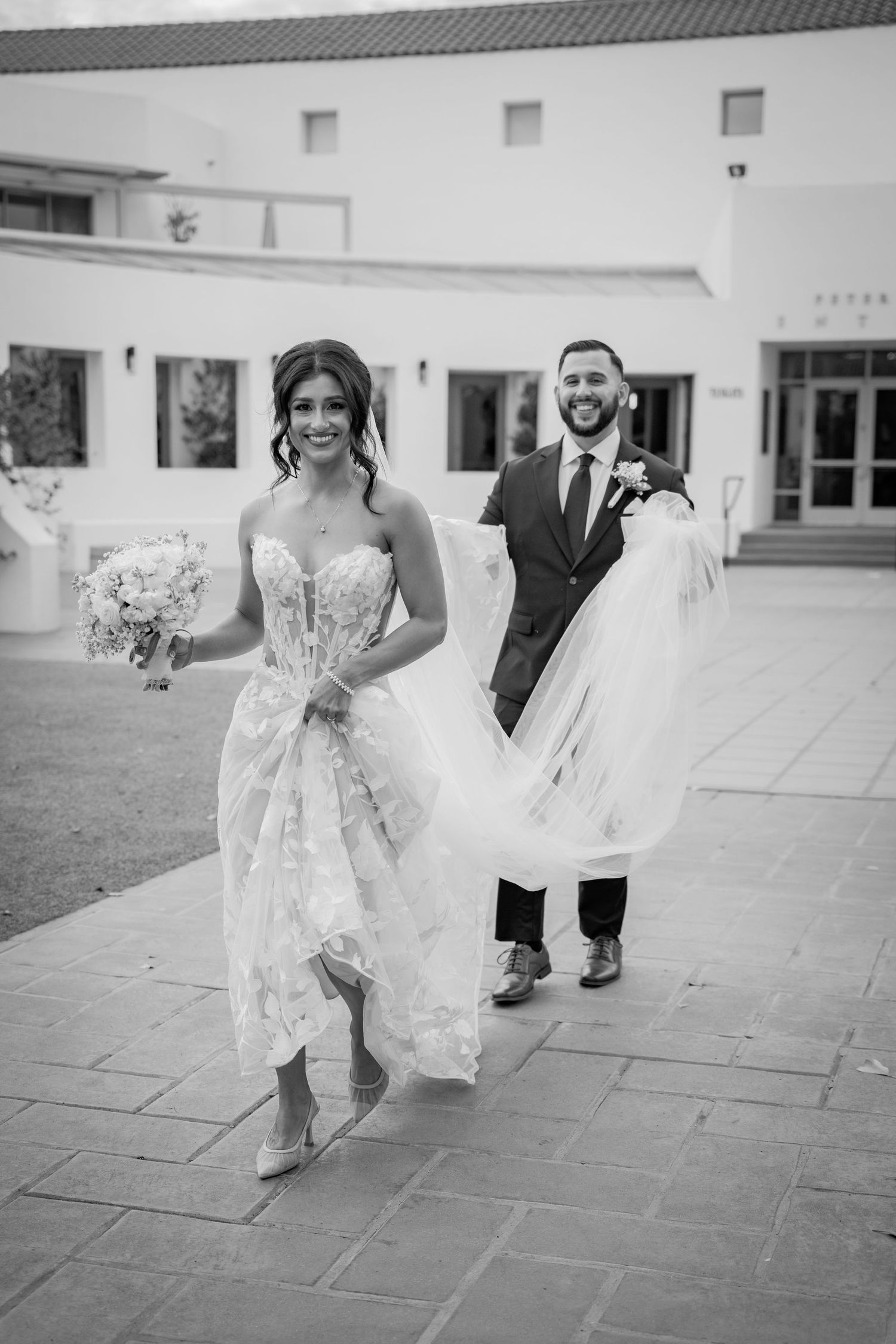 Wedding party members in formal attire walking and laughing together on an outdoor stone patio.