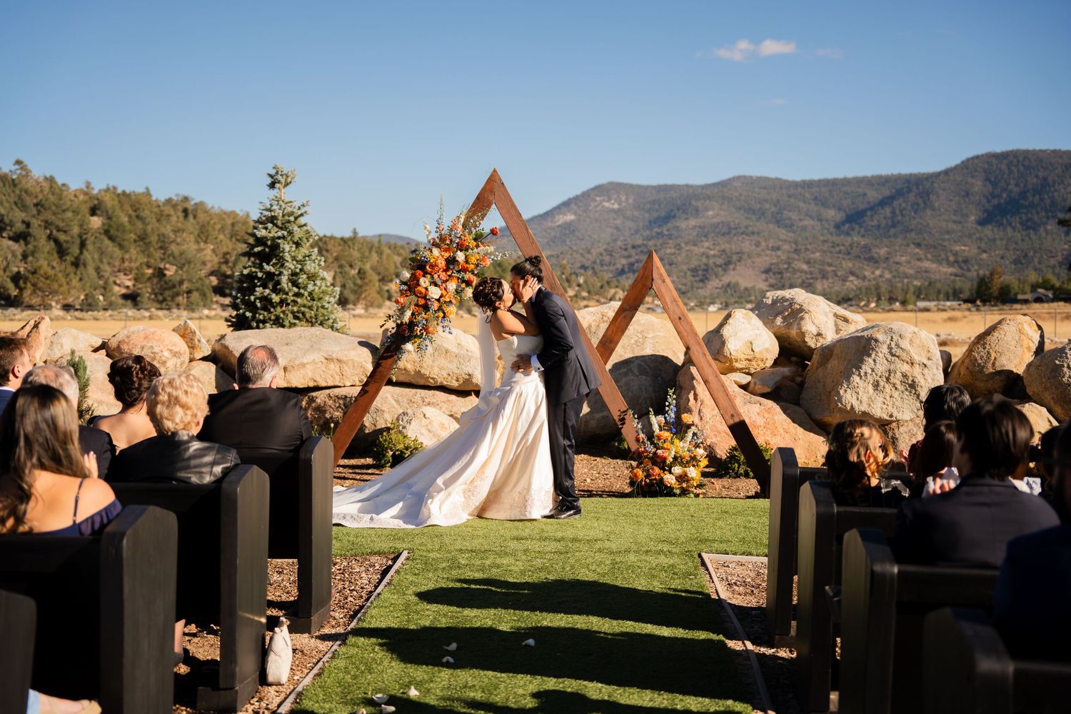A row of large stone sculptures on pedestals overlooks a scenic mountain landscape on a sunny day.