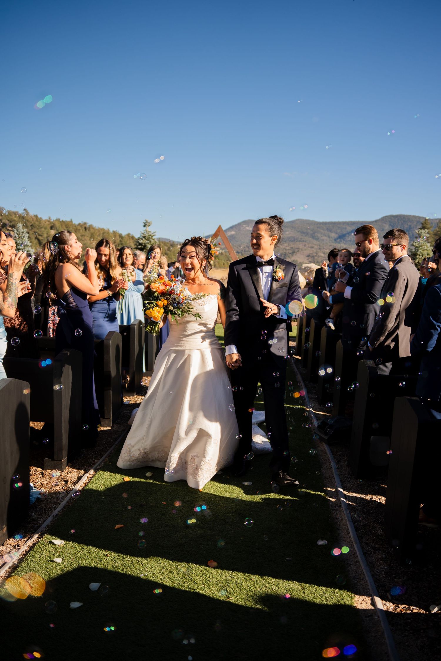 Wedding celebration on a hilltop with confetti flying through the air as guests gather around on a sunny day.