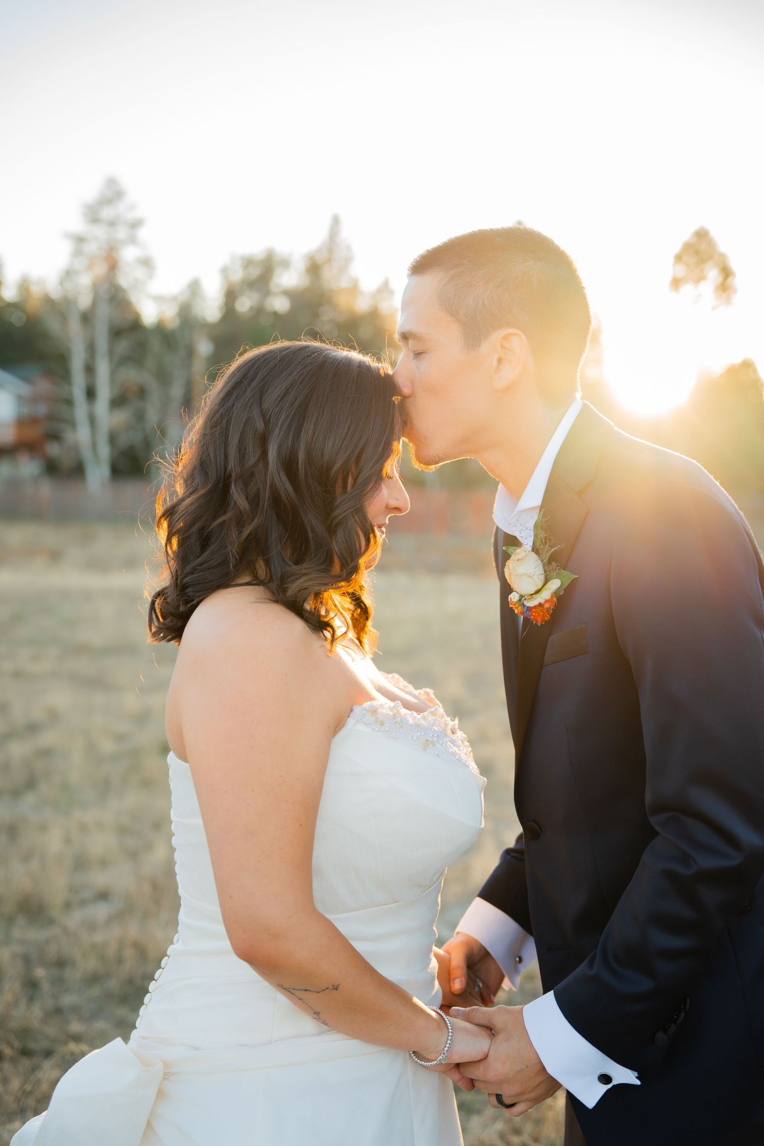 A couple in wedding attire shares an intimate moment at sunset in a rustic outdoor setting.