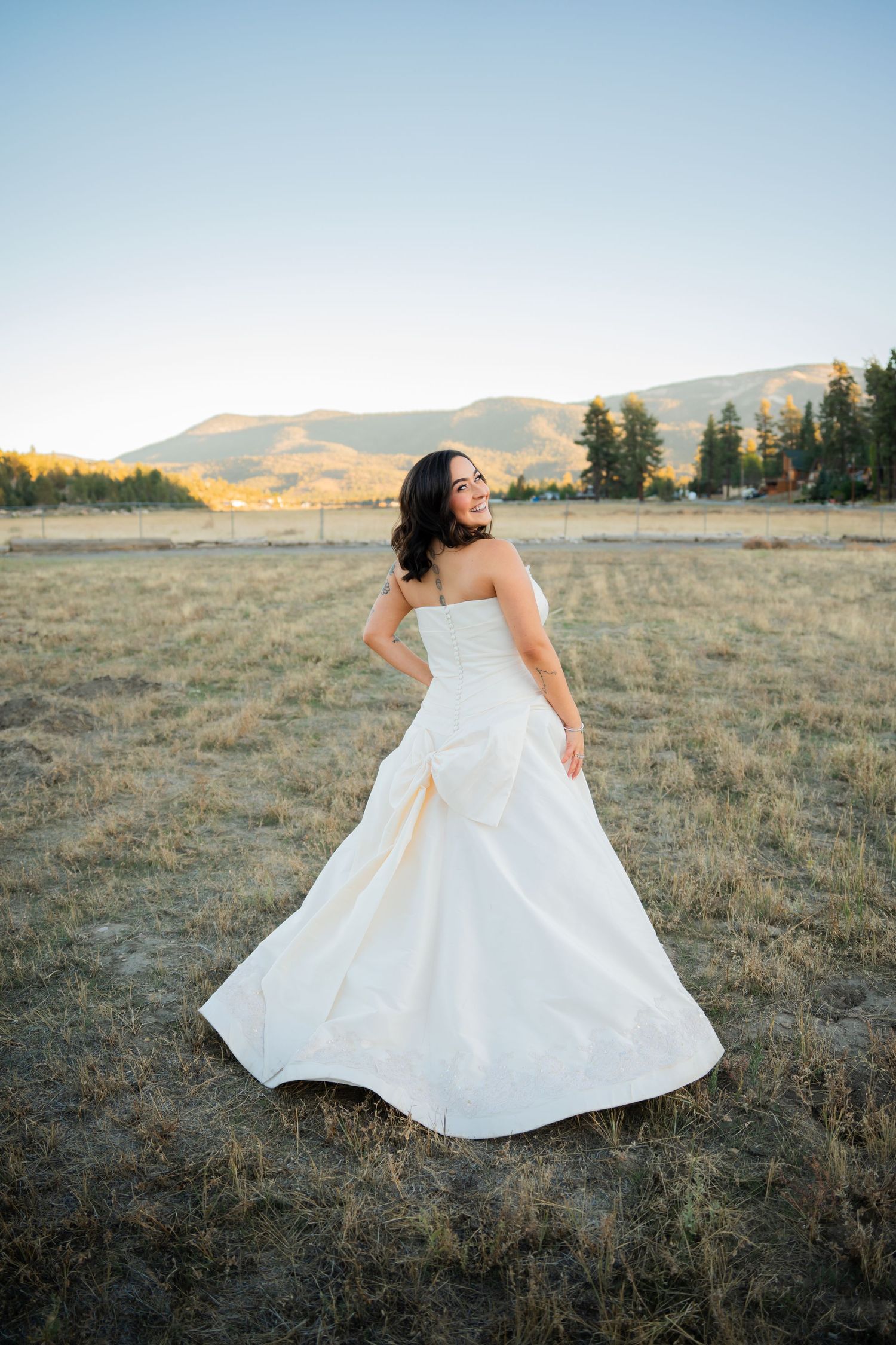 A flowing white wedding dress twirls gracefully across a golden mountain meadow at sunset.