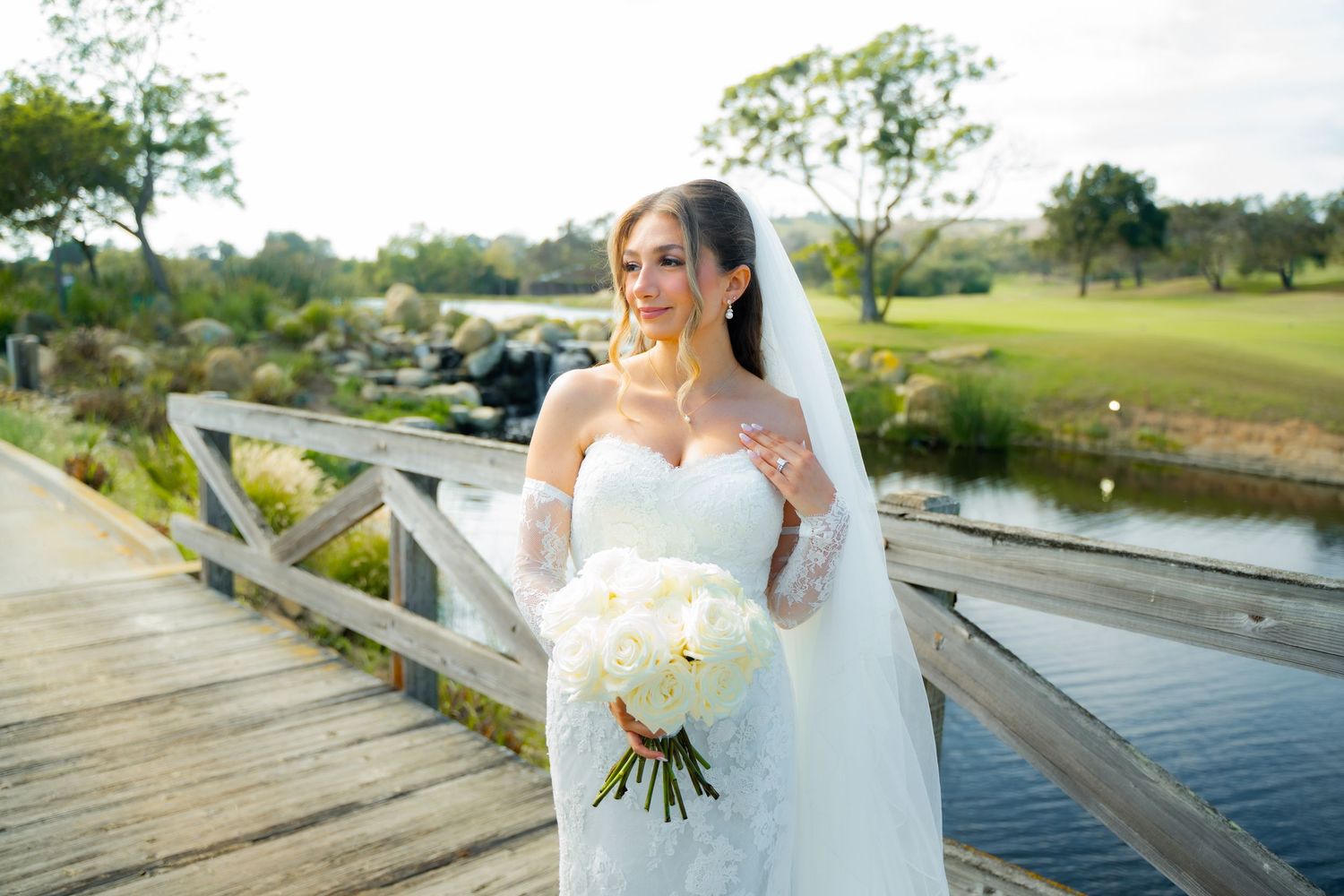 A bride in a white wedding gown poses on a wooden dock overlooking a serene lake on her special day.