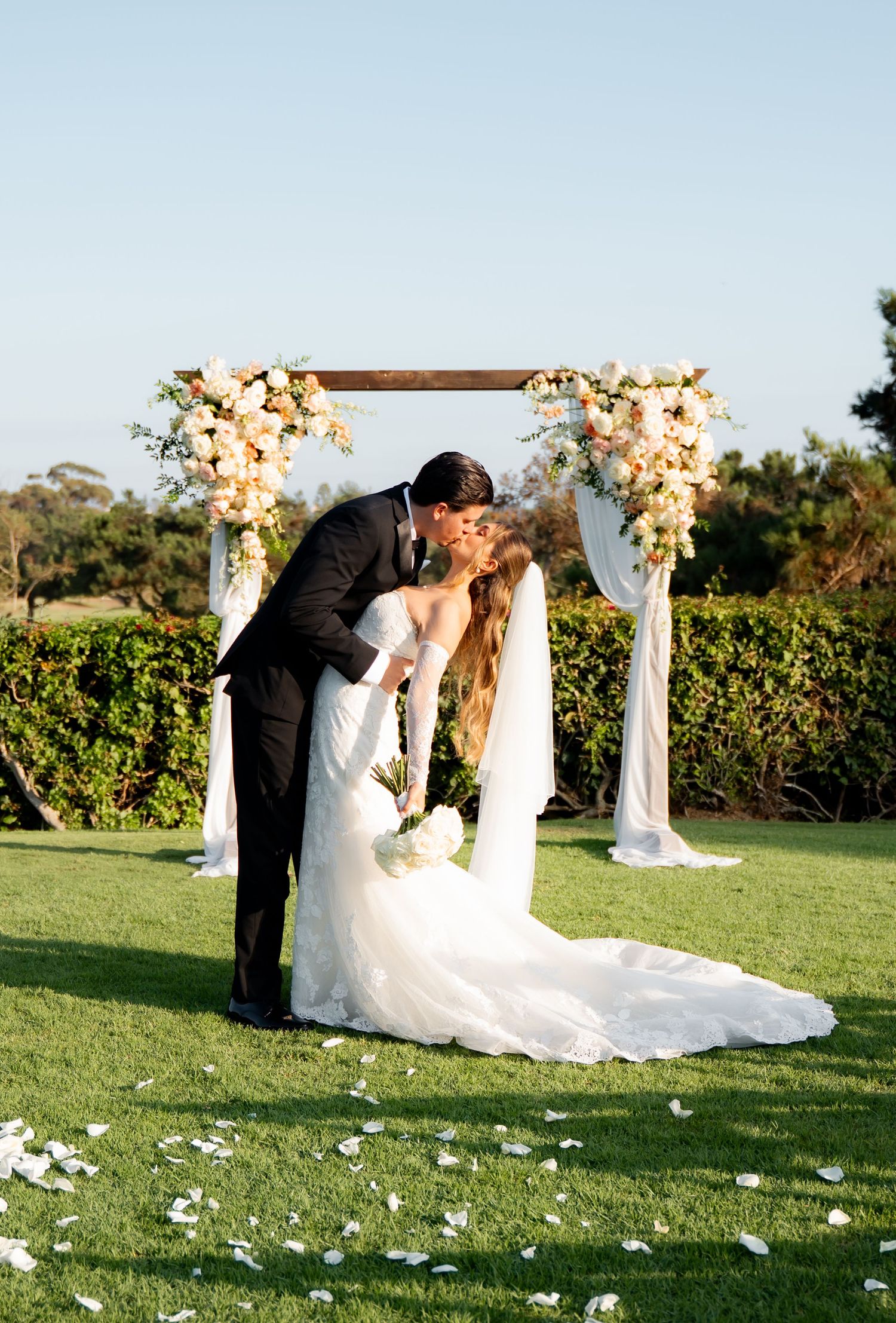 A romantic wedding ceremony sequence captured at sunset on a grassy lawn with white floral decorations and draped arbor.
