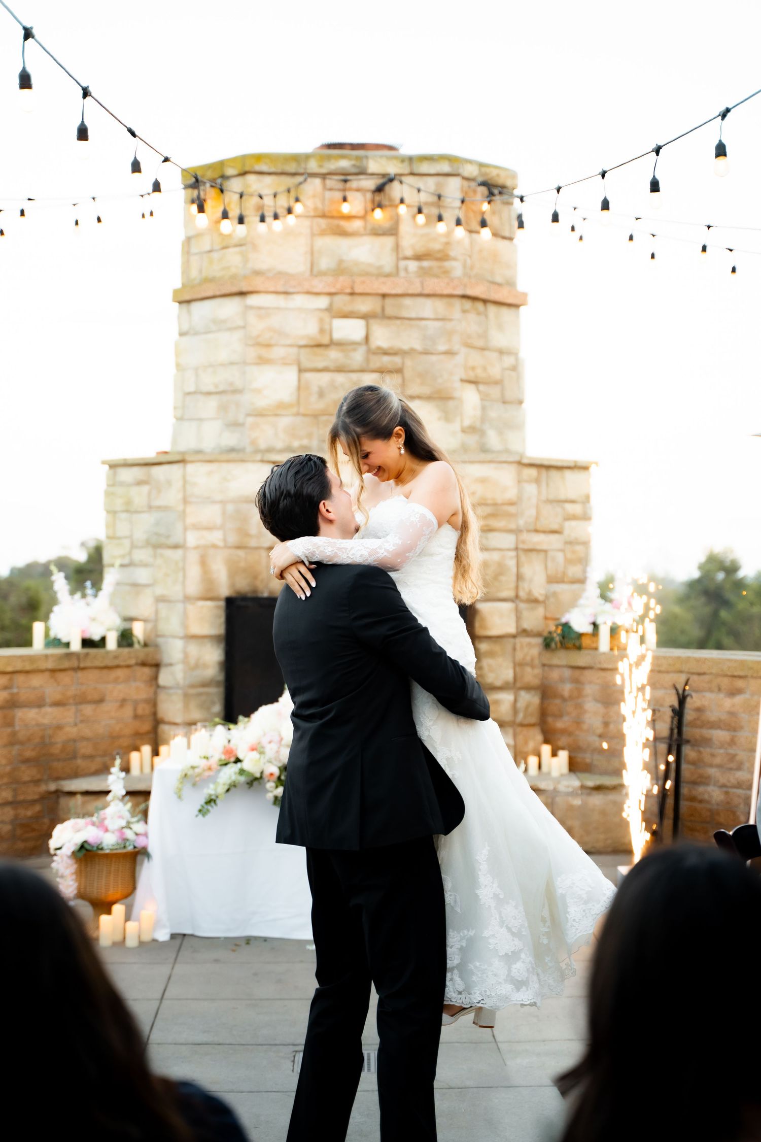 A romantic first dance between newlyweds at an outdoor stone venue with string lights at sunset.