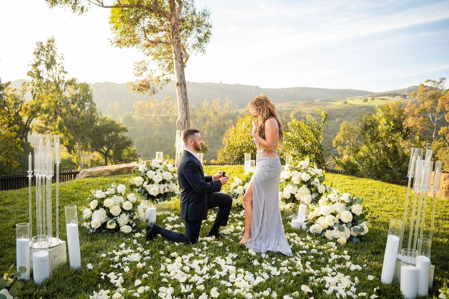 Couple embracing in an elegant outdoor setting with white floral arrangements and mountain views.