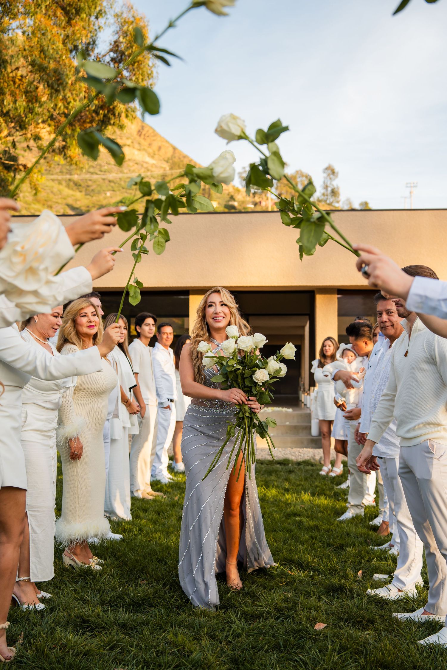 Wedding guests dressed in all white celebrate outdoors during a golden sunset ceremony.