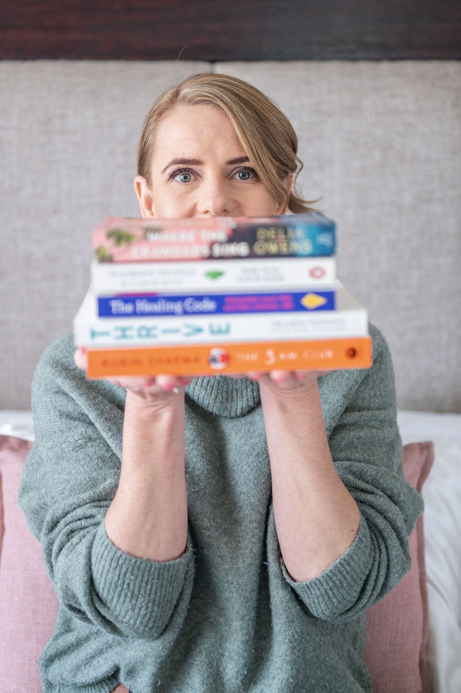 An image showing woman holding stack of books at against a gray background.