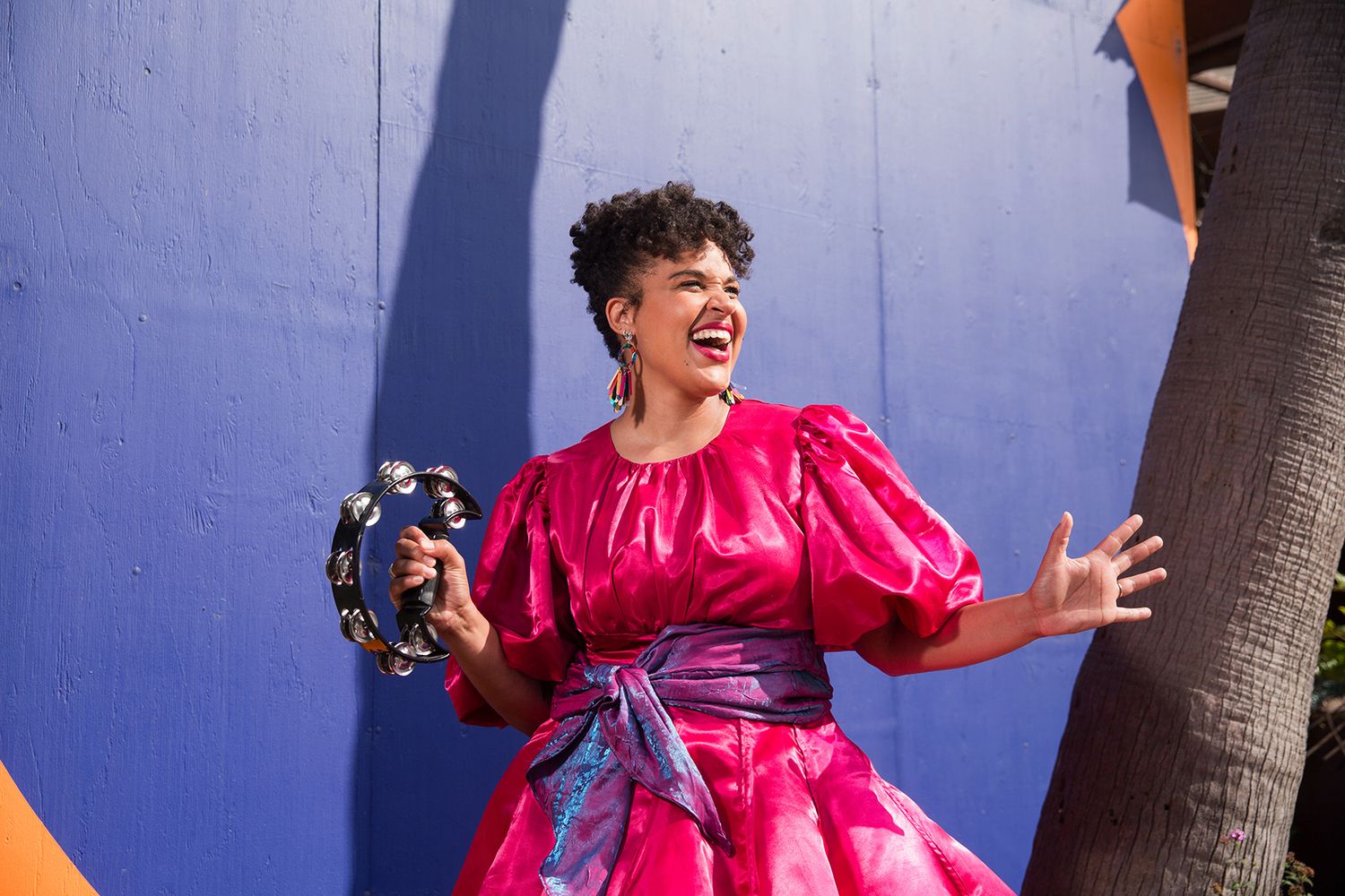 Benefits of a Los Angeles Brand Photographer. Energetic photo showing someone in bright pink outfit posing against blue wall outdoors.