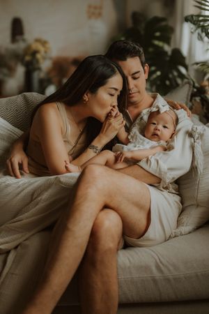 Tender family portrait showing parents and baby sharing affectionate moments on a cozy couch.