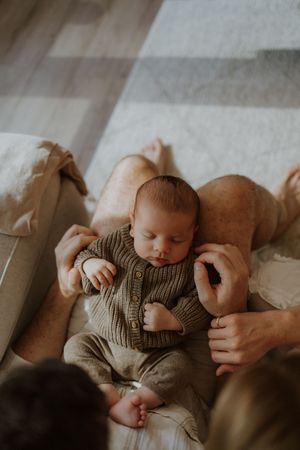 A sleeping baby in a striped onesie lies peacefully on a soft couch in muted lighting.