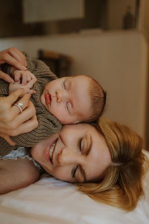 A tender moment captured of a parent and baby in matching sweaters resting peacefully together on white bedding.