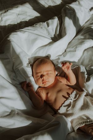Peaceful sleeping baby lying on white bedding in soft natural lighting.