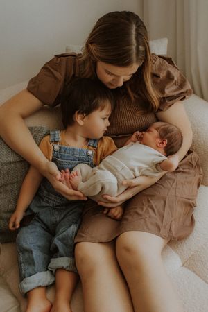 A tender family moment as siblings share cuddles and bonding time with a newborn baby on a cozy bed.