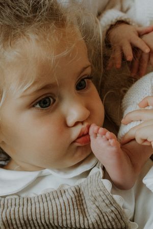 A young child in a knit sweater gazes with bright eyes while sucking their thumb.