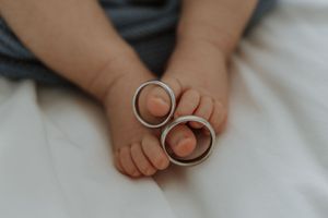 Close-up of baby feet with two silver wedding rings resting between tiny toes on a white blanket.