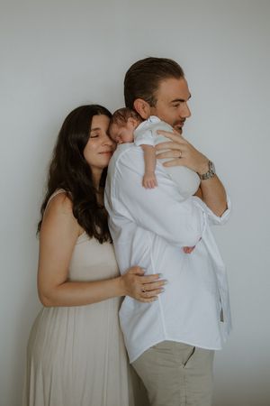 A couple tenderly holds their newborn baby, the mother in a beige dress leaning close as the father cradles the infant.