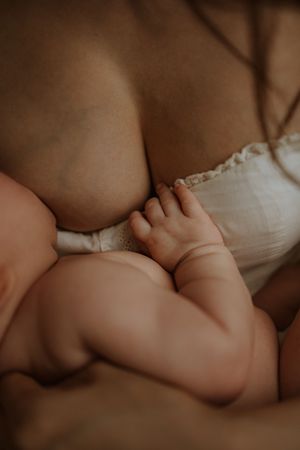 Close-up of a baby's tiny hand grasping while nursing in soft lighting with white fabric.