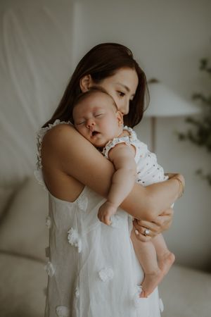 A gentle embrace between parent and child in white clothing against a soft neutral background.