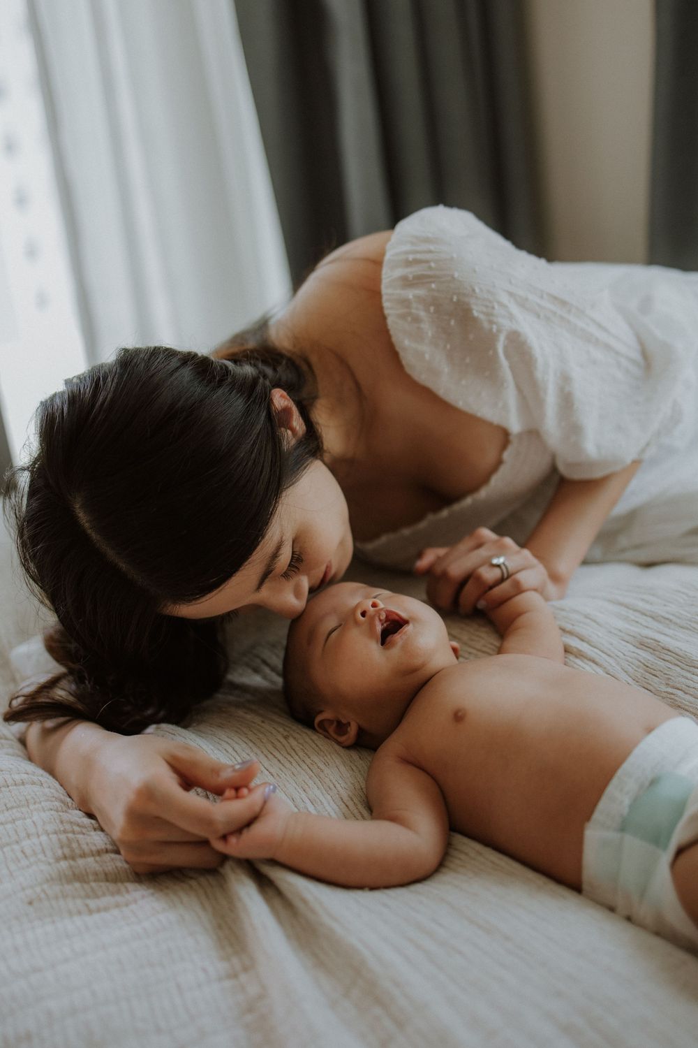 A mother tenderly kisses her newborn baby lying on a bed, sharing a sweet bonding moment.