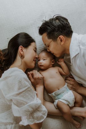 Parents lovingly kissing their newborn baby lying on a soft blanket in a tender family portrait.