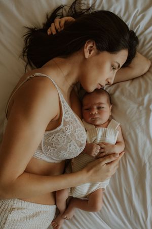 A tender moment between mother and newborn baby snuggled together on white bedding.