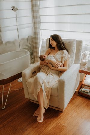 A gentle scene in a serene nursery with soft light showing a tender moment of breastfeeding in a cozy armchair.