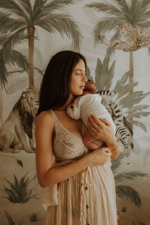 A nurturing moment captured against a tropical mural backdrop as a baby is held close in a gentle embrace.