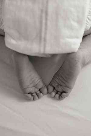 Black and white close-up of newborn baby feet resting on a soft white blanket.