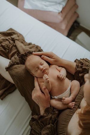 Newborn baby sleeping peacefully on brown linen fabric while parents gently cradle their infant.