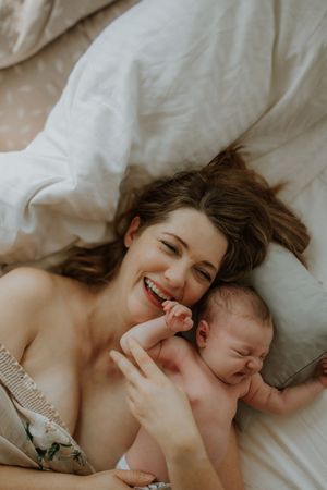A tender moment captured between parent and newborn baby lying together on white bedding.