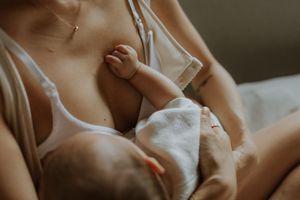 Intimate close-up view of breastfeeding with baby's hand resting against parent in soft natural lighting.
