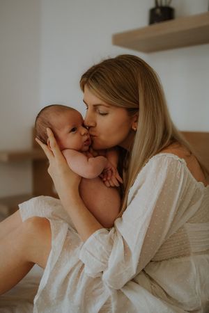 A tender moment between mother and newborn baby in soft warm lighting against a neutral background.
