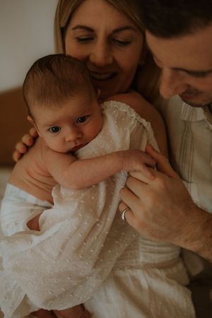 A tender moment between parent and baby in white clothing, captured in a warm-toned collage of intimate photographs.