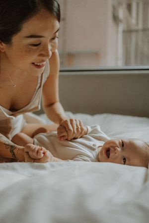 A tender moment between mother and baby lying on white bedding in warm natural lighting.