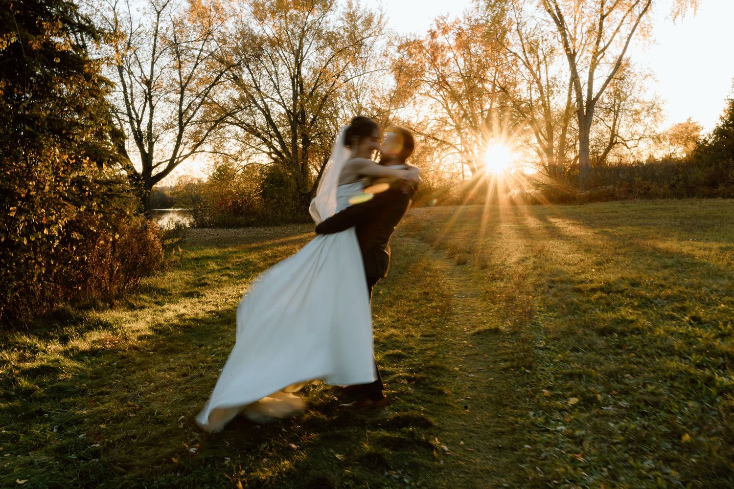 Two figures embrace in a romantic backlit wedding photo during golden hour sunset in an autumn field.