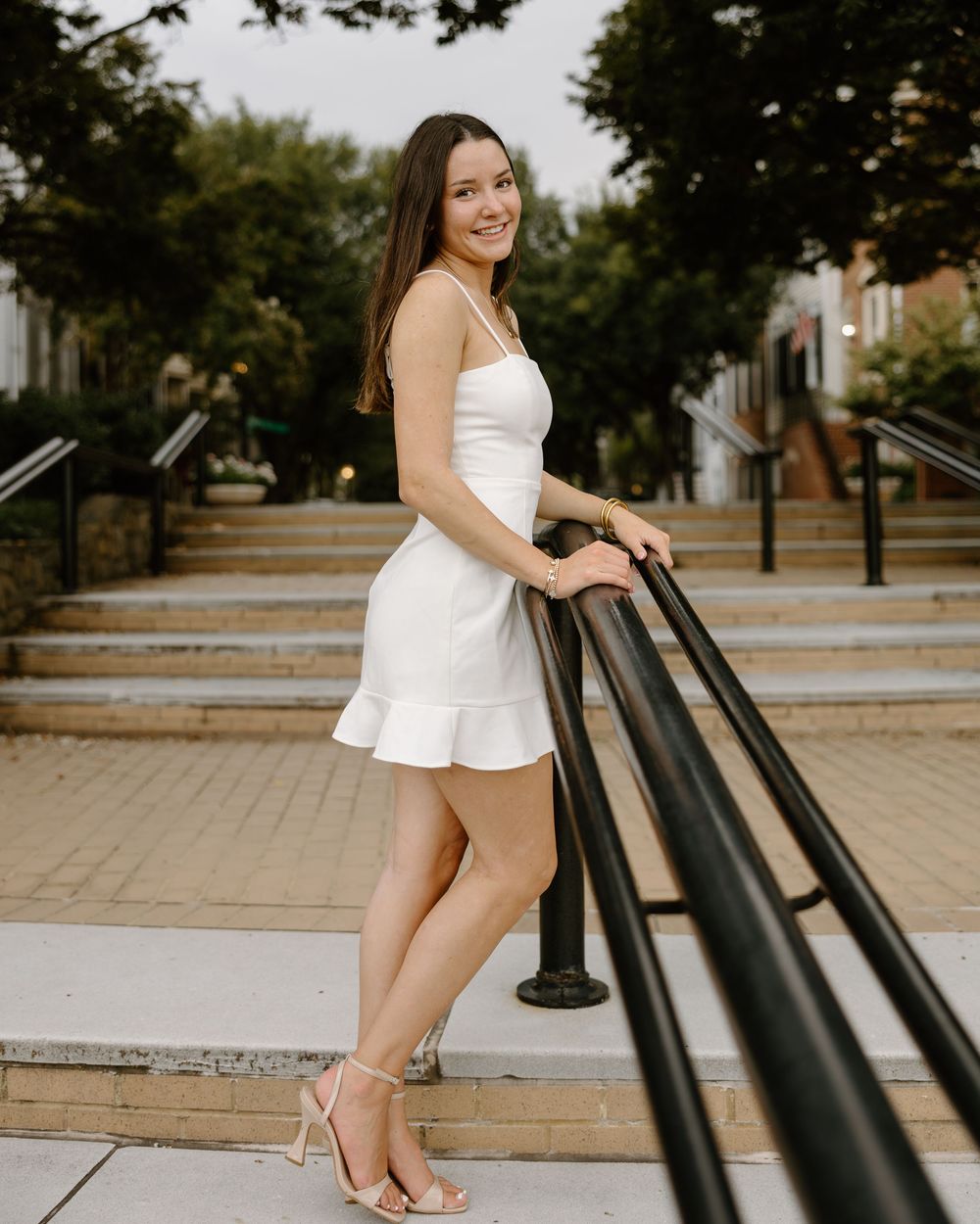 A woman in a white dress poses playfully on outdoor steps in a warm summer setting.