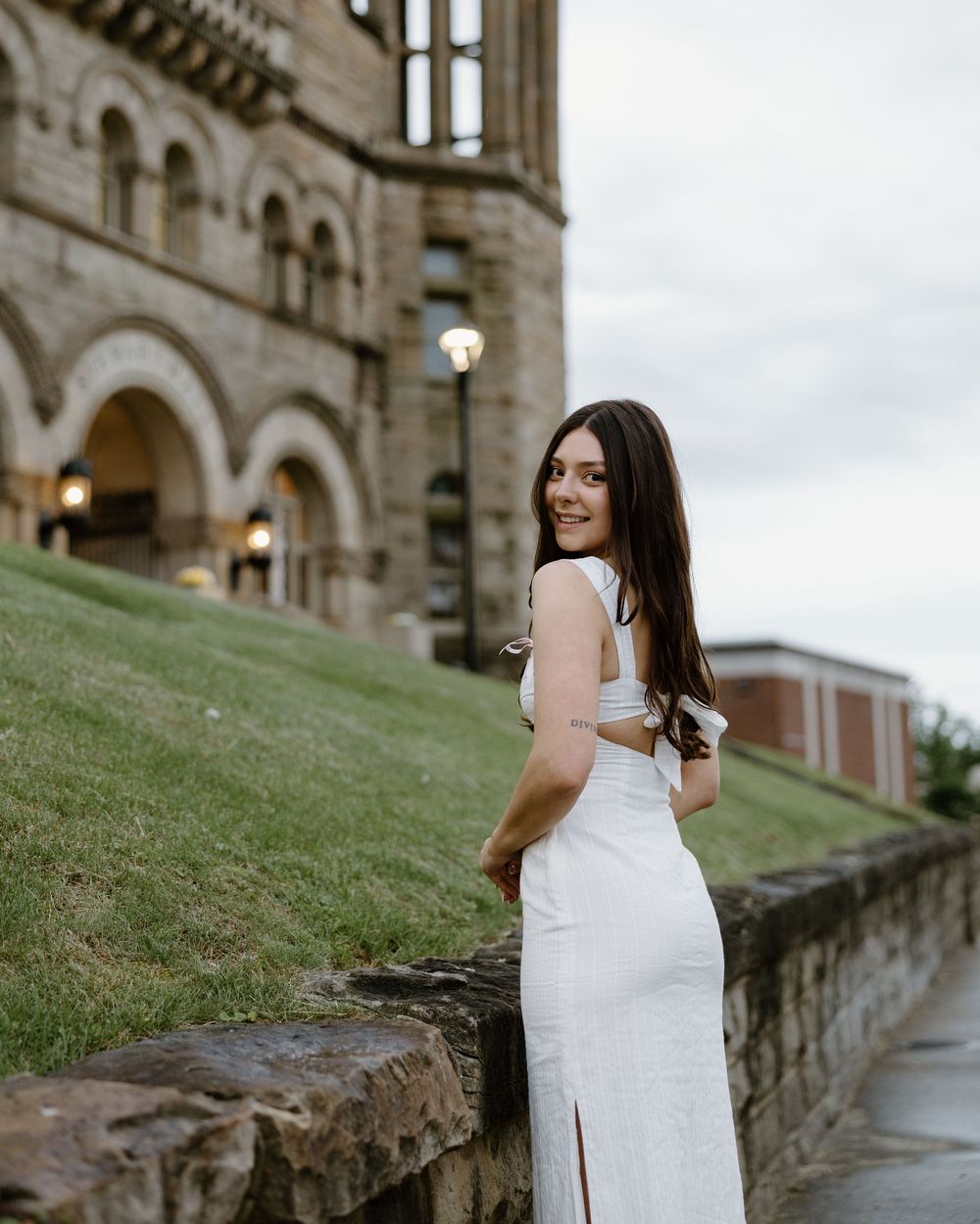 A person in a white dress poses on stone steps outside a grand historic building with Gothic architecture.