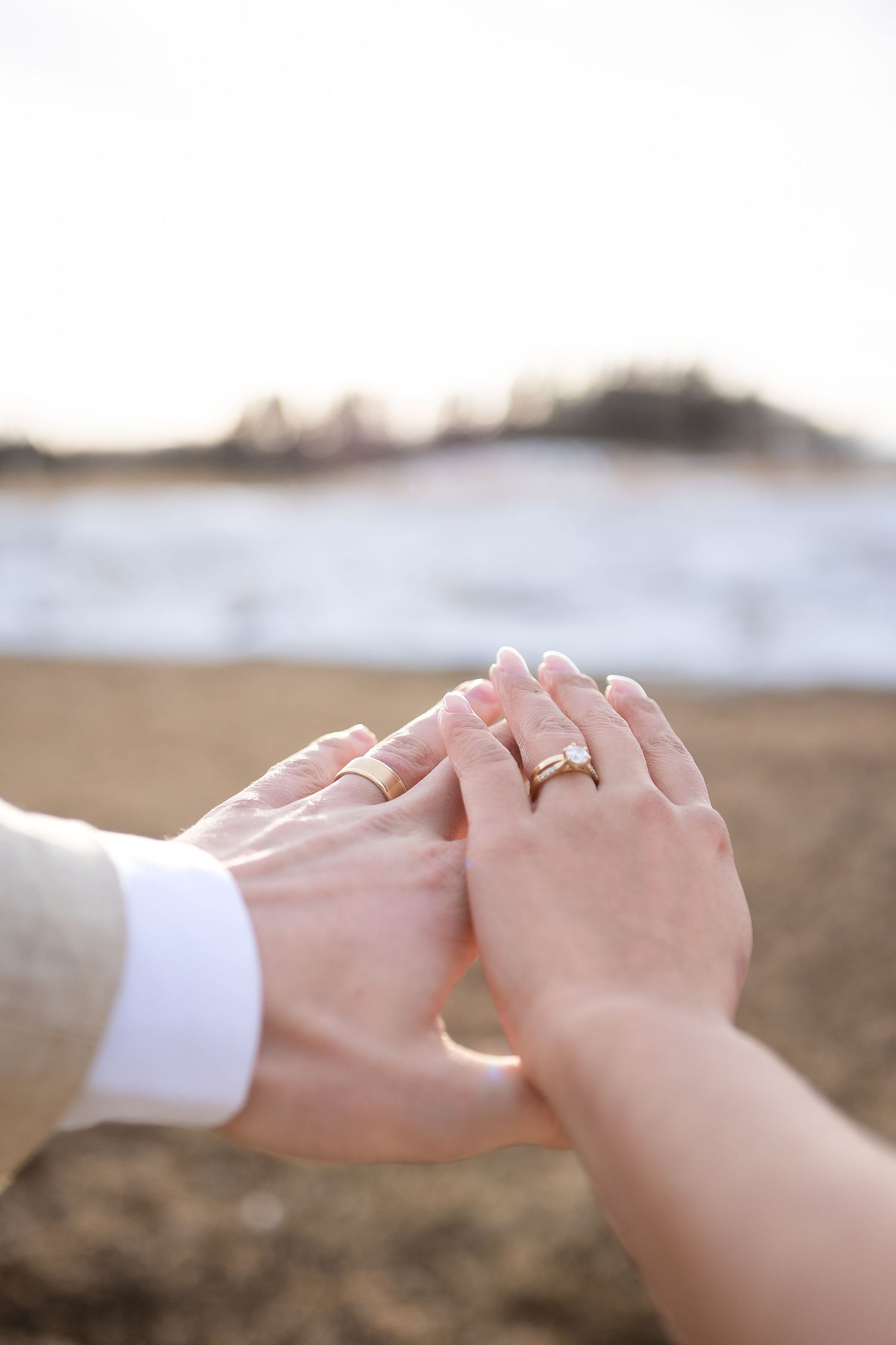 Close-up of newlyweds holding hands with engagement ring visible.