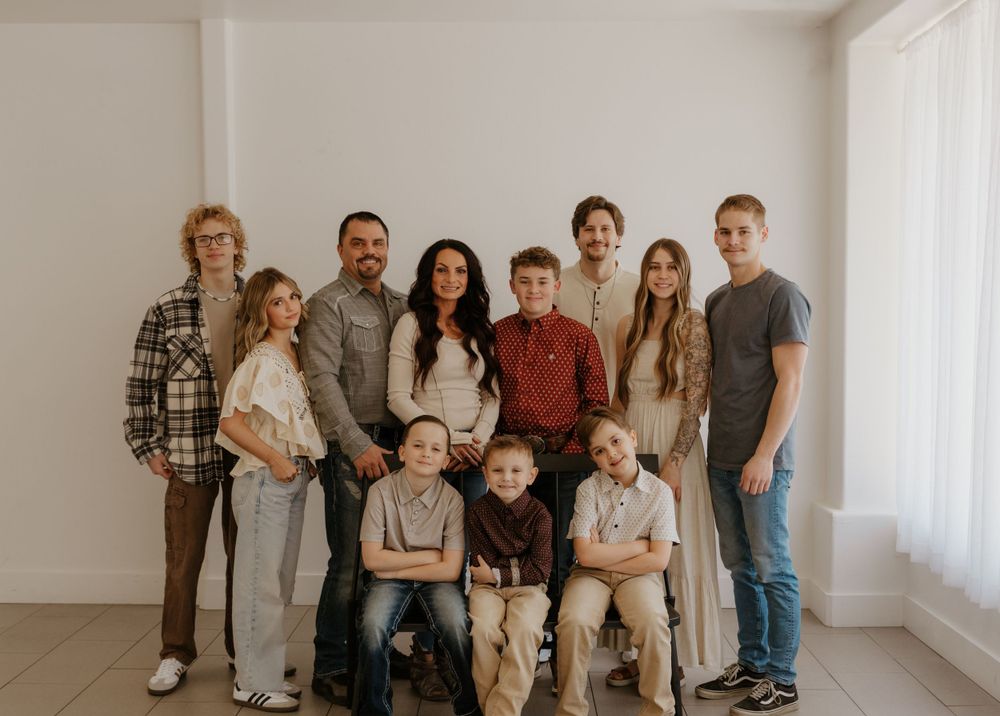 Large group portrait of people lined up against a white wall in coordinated neutral-colored outfits.