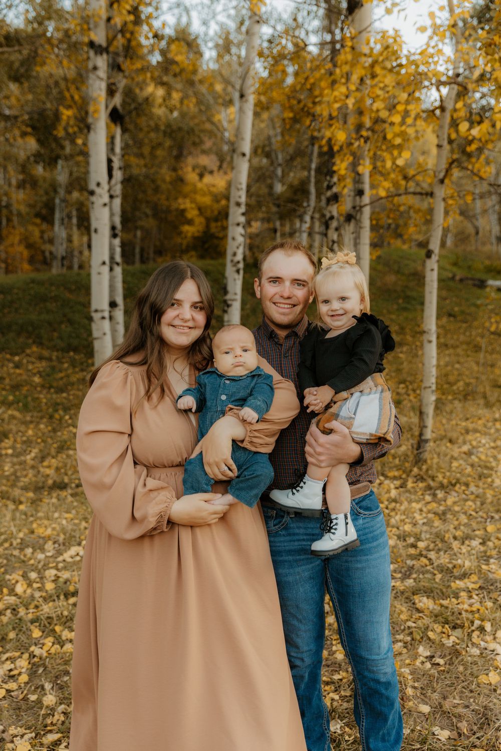 Family portrait in autumn setting with golden aspen trees and fallen leaves.