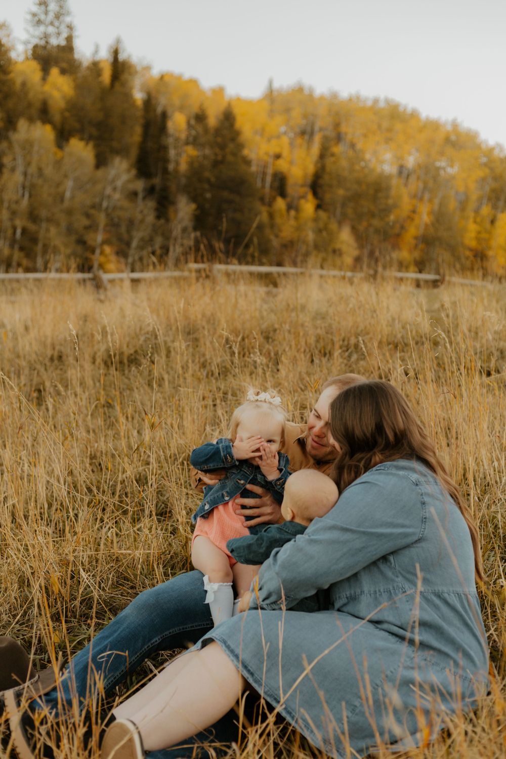 A family lying in golden autumn grass taking photos together in a playful manner.