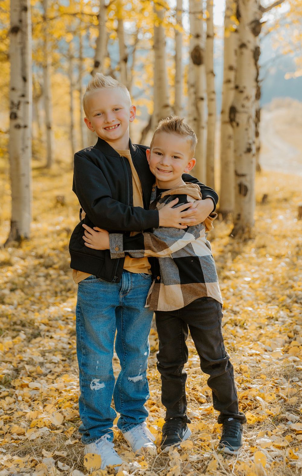 Young siblings hugging and playing among yellow aspen trees in autumn.