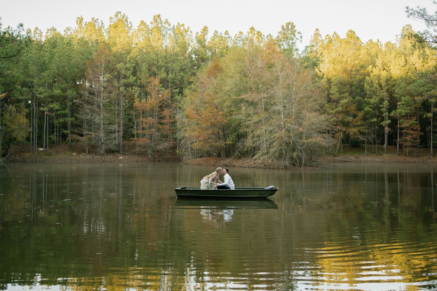 Small boat floats peacefully on a still lake surrounded by autumn trees with golden foliage reflecting in the water.