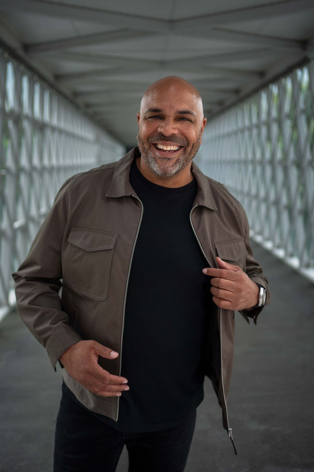 Person wearing brown jacket smiling warmly in modern white corridor.